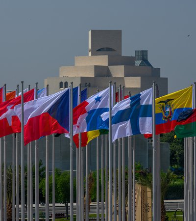 International flags on high poles with a geometric, pyramid-like building in the background.