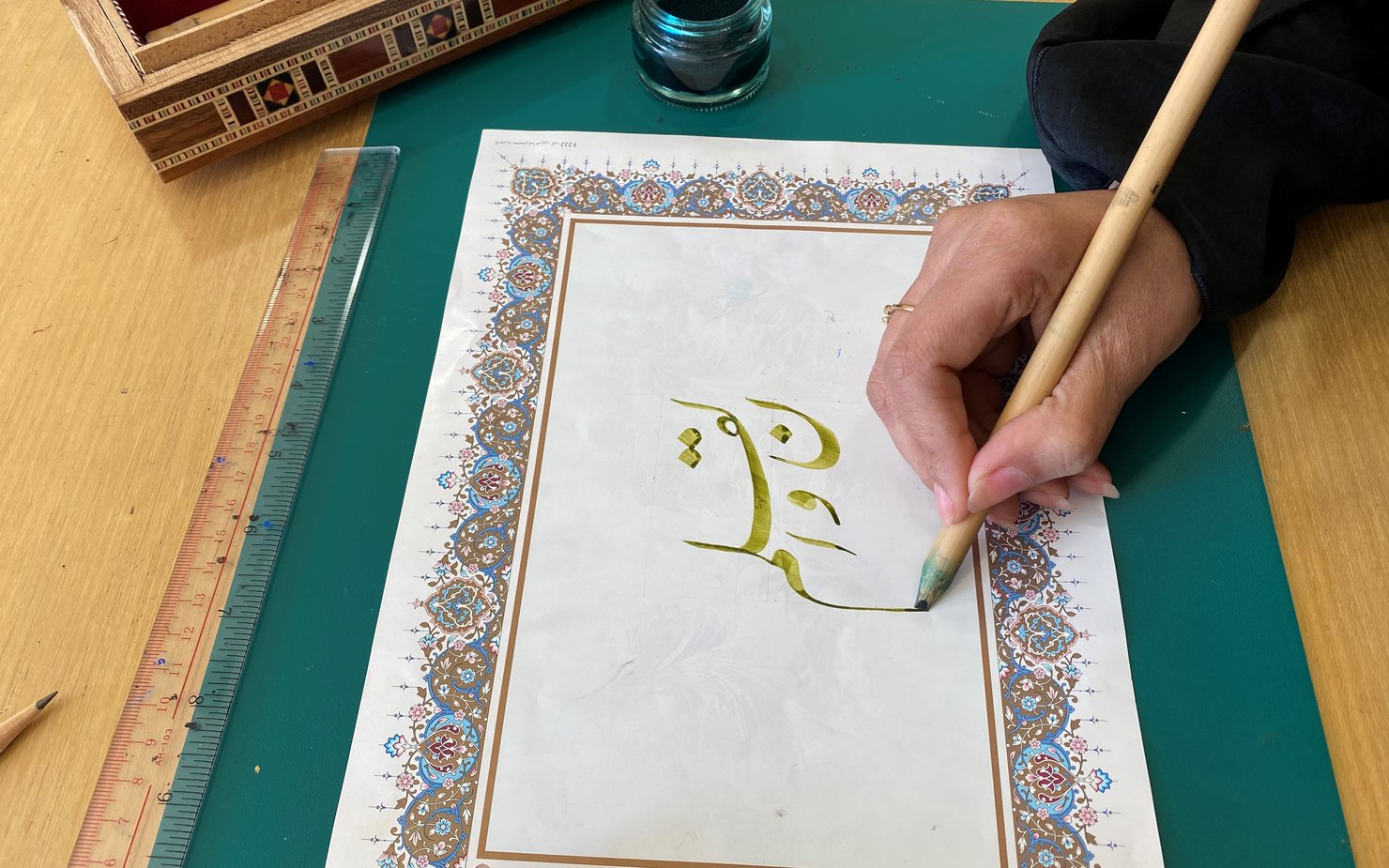 Hand holding a pen and writing in Nasta'liq Script