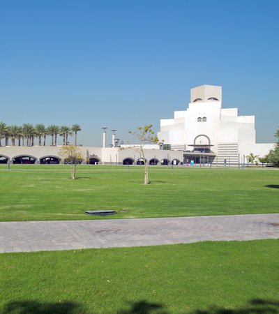 An open parkland space with green grass and native trees and the Museum of Islamic Art in the background