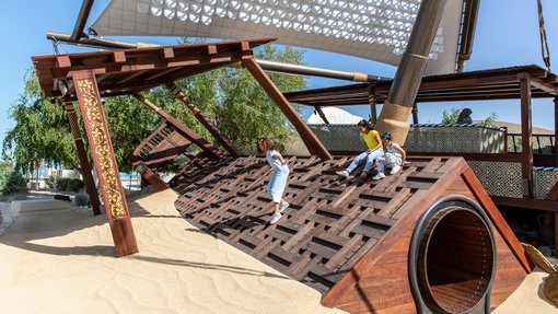 Three children having fun as they play on the wooden boats in the Nakilat Adventure Ship playground at NMoQ