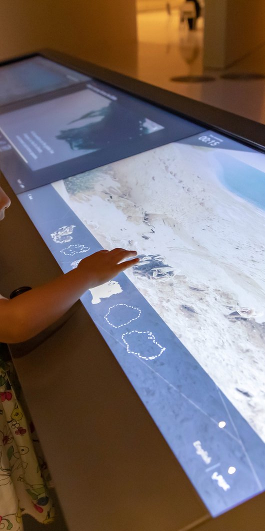 A little girl interacting with a digital gallery display at the National Museum of Qatar.