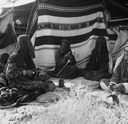 Three women spinning yarn inside a tent with an old man sitting next to them