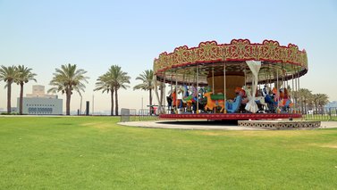 A brightly painted carousel with colourful animals for children to ride, in parkland with MIA in the background