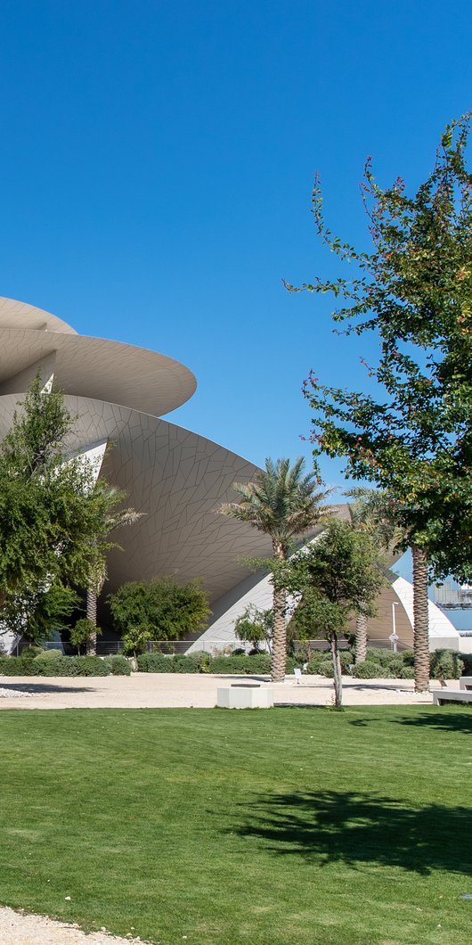 Landscaped gardens with green grass and native plants and trees surrounding the National Museum of Qatar