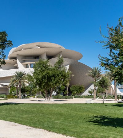 Landscaped gardens with green grass and native plants and trees surrounding the National Museum of Qatar