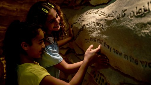 Two smiling children exploring the wall carvings in NMoQ's Cave of Wonders