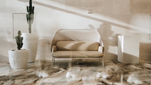 A sandstone coloured interior with small modern sofa and two potted plants.