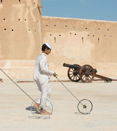 Two boys dressed in traditional Qatari attire hoop rolling with Al Zubarah fort in the background