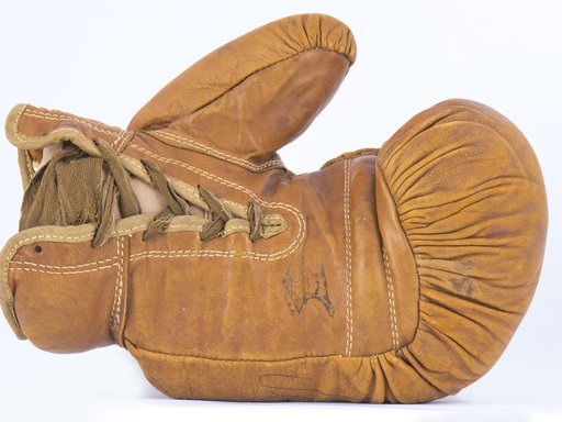 A camel coloured, aged, leather boxing glove lies on its side.