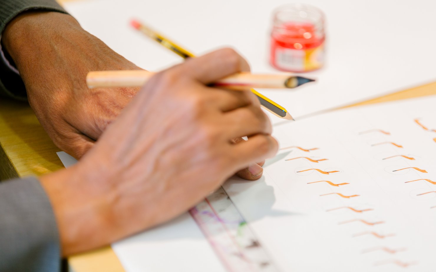 A man with a dip pen in his hand practices Arabic calligraphy on a white piece of paper