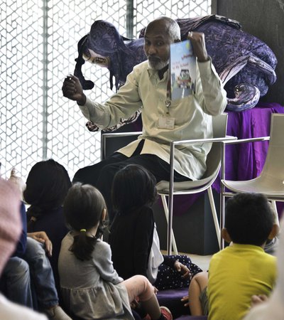 Children sitting down for storytime while a librarian holds up a storybook and gestures towards the children