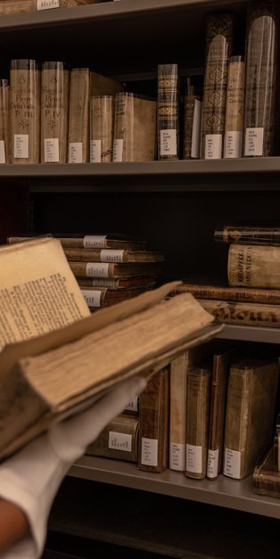 Person wearing white gloves and holding an antique book in front of library book shelves at the Museum of Islamic Art, Qatar