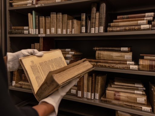 Person wearing white gloves and holding an antique book in front of library book shelves at the Museum of Islamic Art, Qatar