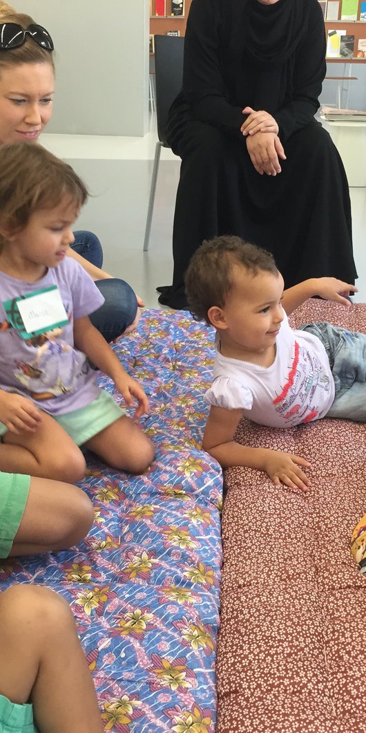 A group of young children and their parents gather while a lady reads a story to them