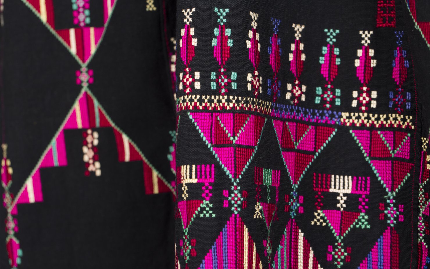 Intricate pink, purple, green and yellow embroidery is shown on rich black material.