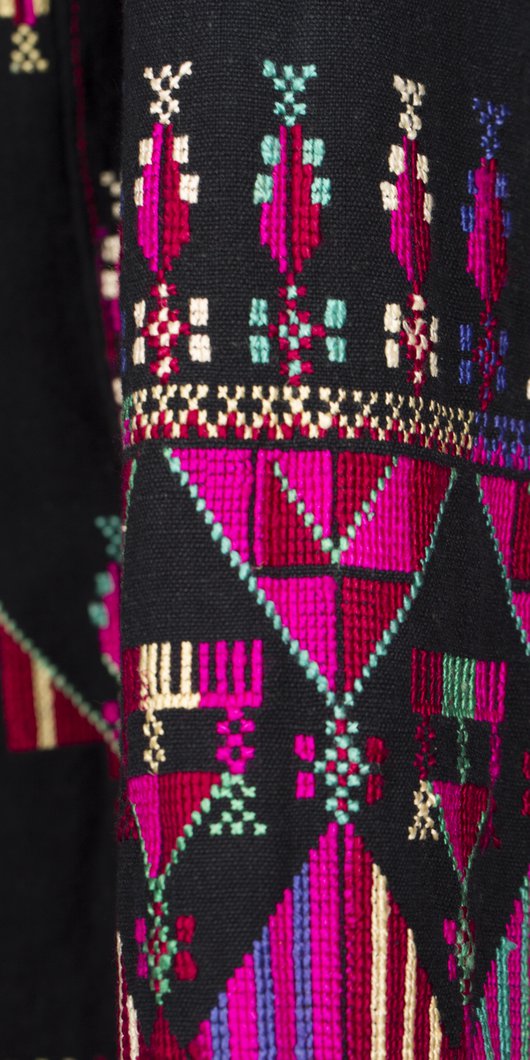 Intricate pink, purple, green and yellow embroidery is shown on rich black material.