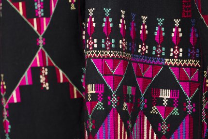 Intricate pink, purple, green and yellow embroidery is shown on rich black material.