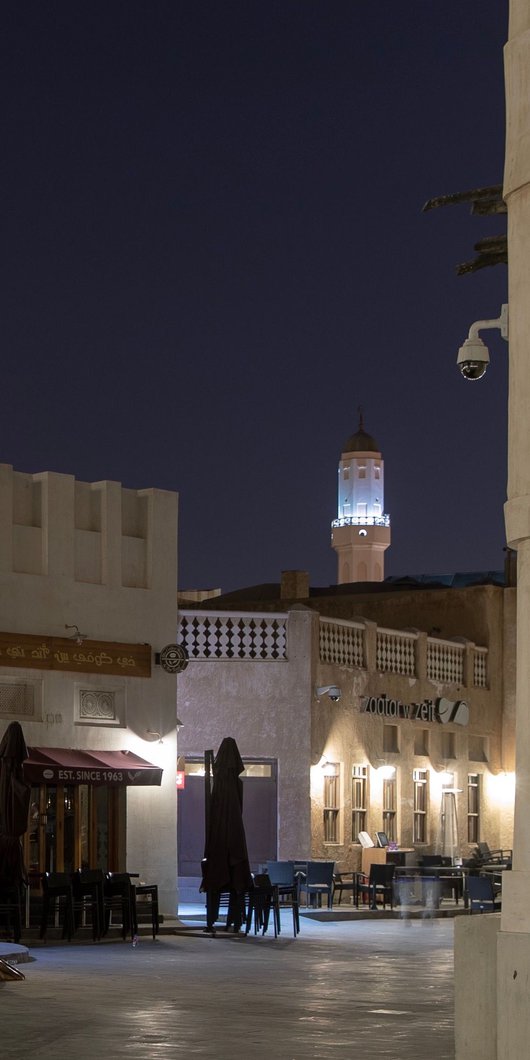 A bronze thumb sculpture in the middle of Souq Waqif, with a number of buildings and cafes in the background.