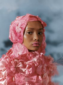 A young black woman with pink lipstick wears a hijab made from large exotic pink flowers.