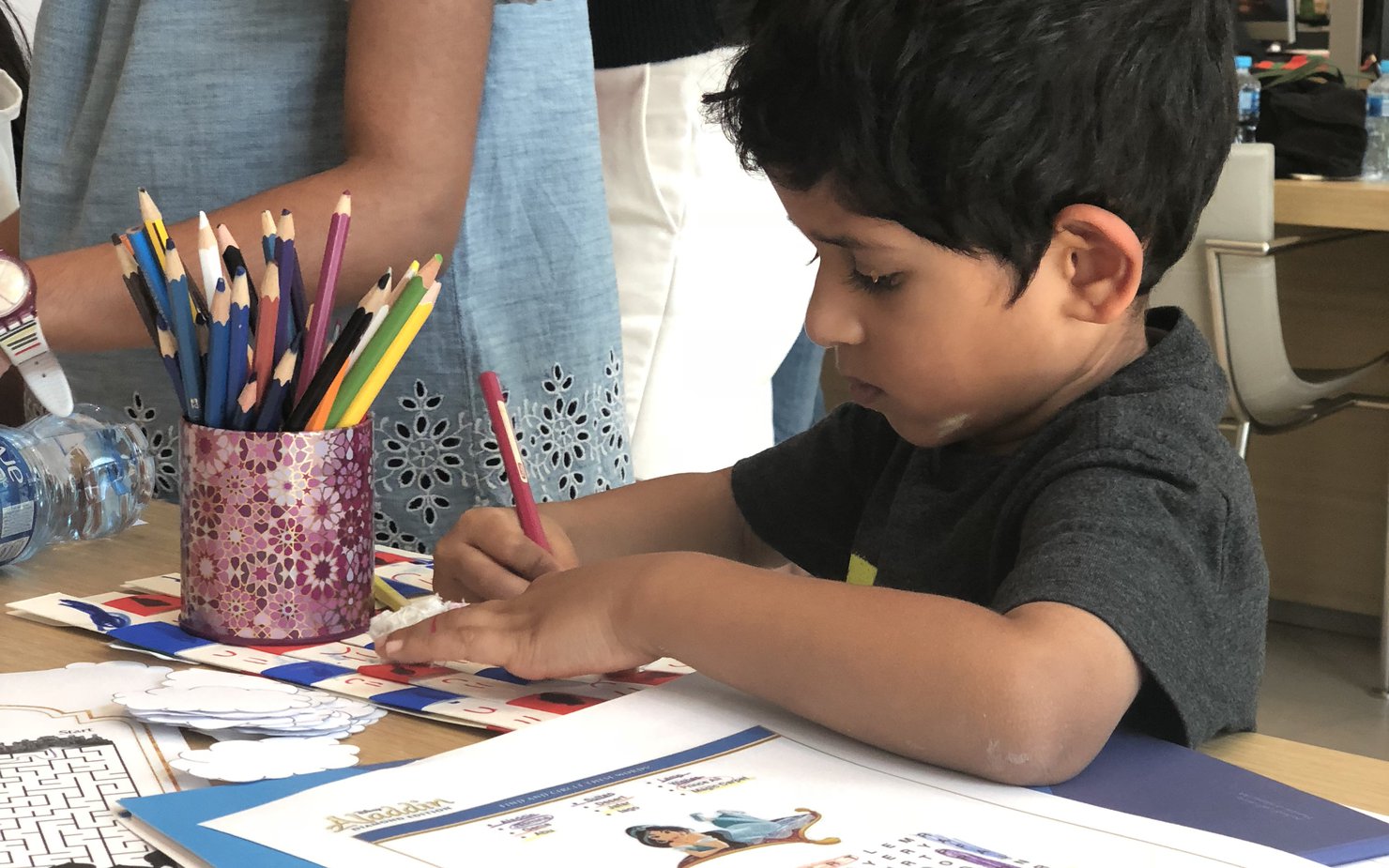 Two children colouring on a piece of paper with coloured pencils and books surrounding the desk