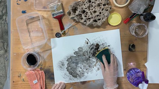 Birds eye view of a workshop participant’s desk with art materials and artwork.